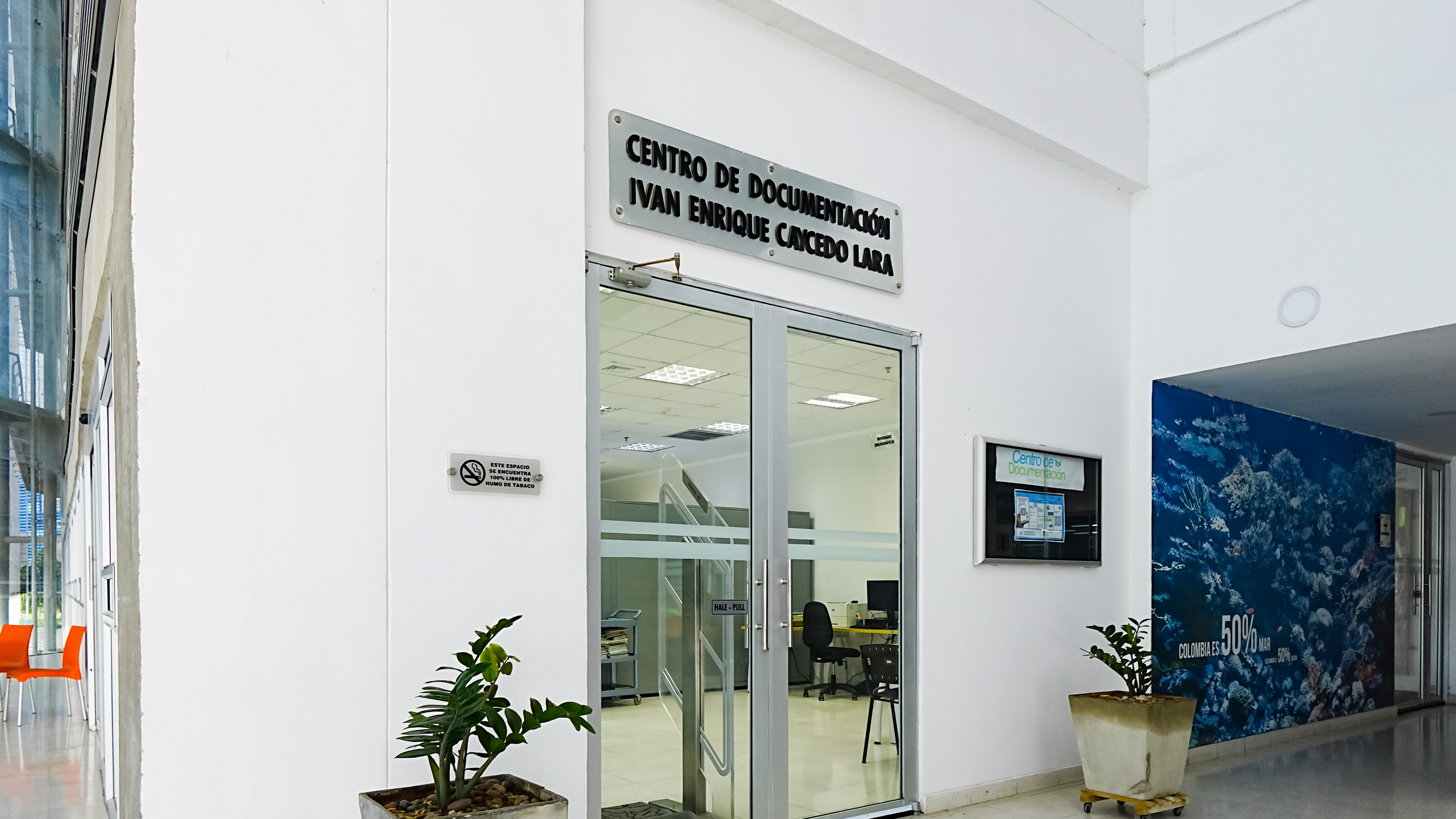 Entrada del Centro de Documentación Iván Enrique Cancedo Lara, con puerta de vidrio, señalización superior, plantas decorativas y vista parcial del interior del centro.