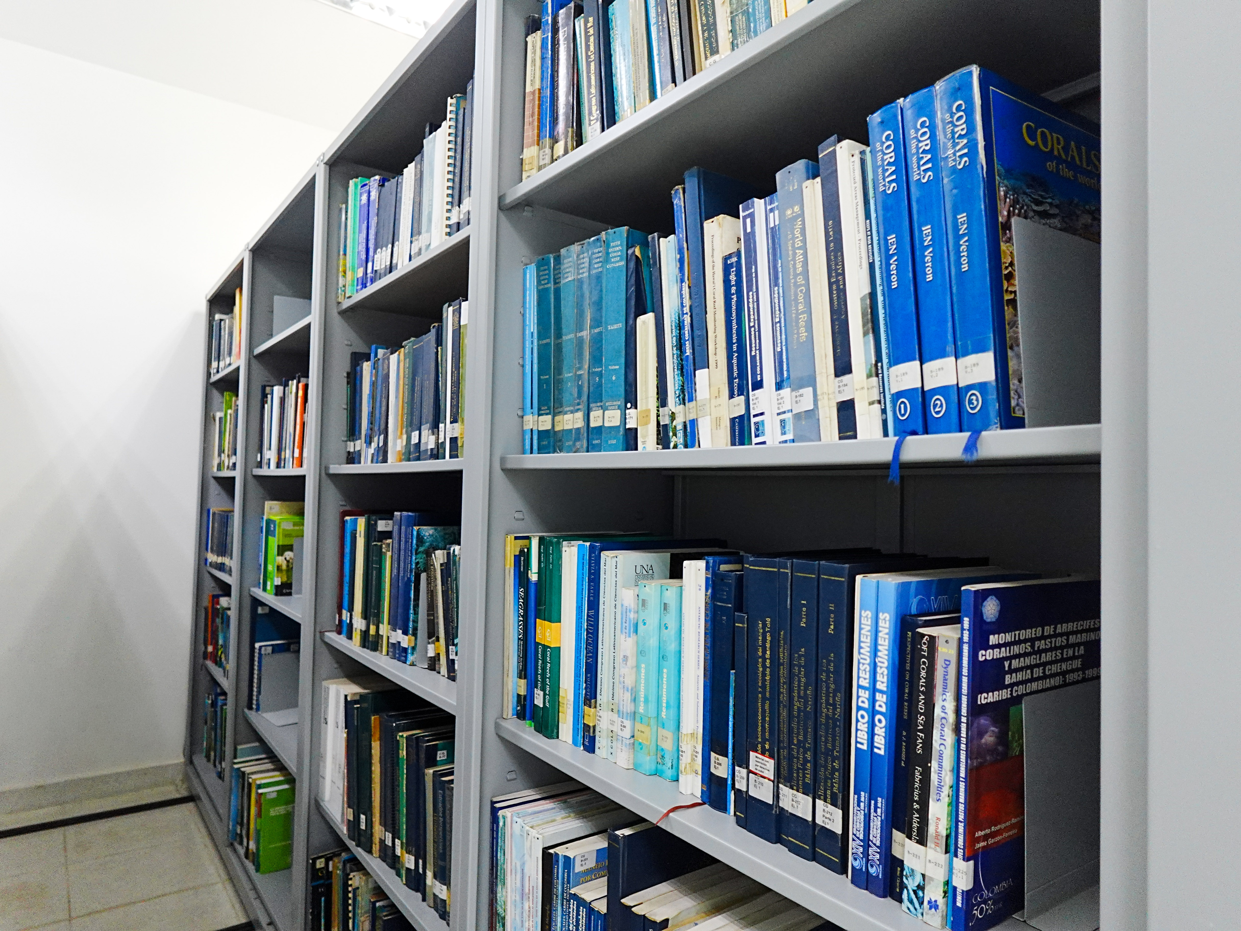 Estanterías del Centro de Documentación con libros especializados en biología marina, arrecifes de coral y temas ambientales, organizados en un pasillo de biblioteca.